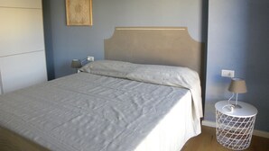 A neatly made bed with a headboard, a bedside lamp, and a small round side table with a lamp. - Only 20 min from Olbia: charming 2-bedroom apartment in San Pantaleo with wifi (San Pantaleo)