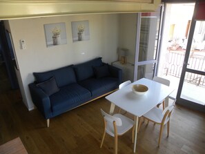 Un salon moderne avec un canapé bleu foncé, une table blanche sur laquelle se trouve un bol, et deux chaises blanches. Deux tableaux encadrés sont accrochés au mur.