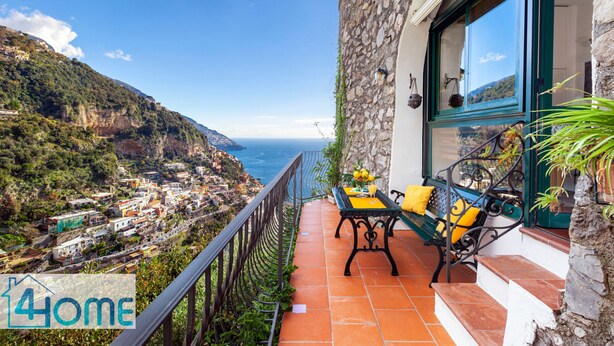 A balcony with a table and chairs overlooking a coastal village.
