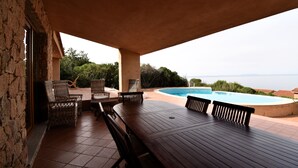 A covered outdoor area with a pool, wicker furniture, and a view of the sea.