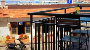 A coastal building with a balcony, a scooter, and a view of the sea and mountains.