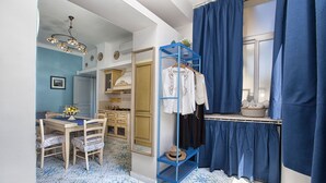 Ein Zimmer mit Esstisch, Stühlen, einem blauen Kleiderständer und einem Fenster mit blauen Vorhängen.
