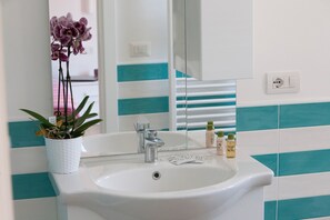 Ein Badezimmer mit einem weißen Waschbecken, einem Spiegel, einer Topf-Orchidee und Pflegeprodukten auf der Ablagefläche.