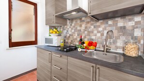 Una cocina moderna con armarios de madera, microondas, pileta y una variedad de frutas y verduras frescas en la encimera.