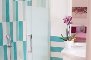 Ein Badezimmer mit türkisfarbenen und weißen Fliesen, einer Dusche und einer Orchidee im Blumentopf auf der Ablagefläche.