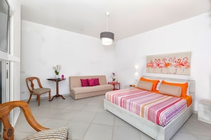 Ein Schlafzimmer mit Bett, einer Couch, einem Sessel, einem kleinen Tisch und einem Gemälde an der Wand.