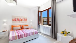 Une chambre à coucher avec un lit, une table de chevet, une petite table sur laquelle se trouvent une bouteille et des citrons, une chaise, une fenêtre avec des rideaux et un téléviseur fixé au mur.