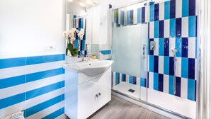 Une salle de bain moderne avec un lavabo blanc, un miroir et des carreaux à rayures bleues.