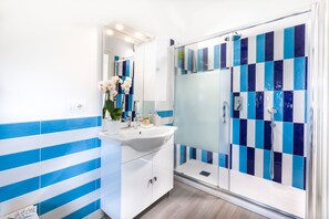 Casa de banho moderna com lavatório branco, espelho e azulejos listados em azul.