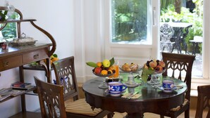 Een eettafel met stoelen, een fruitschaal, een koffiekop en een raam met uitzicht op groen.