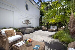 Eine Terrasse mit Korbmöbeln, einem Steinfountain und üppiger Bepflanzung.