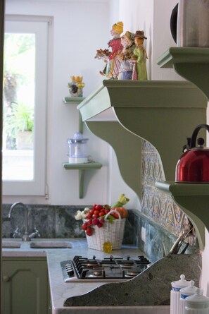 Une cuisine équipée d’une cuisinière à gaz, d’une bouilloire rouge et d’un panier de fruits posé sur le comptoir.