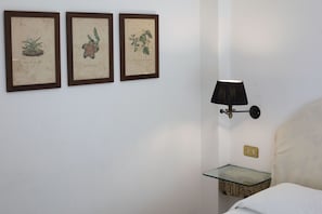 Ein Zimmer mit einem Bett, einem Nachttisch mit Lampe und drei gerahmten Pflanzenbildern an der Wand.