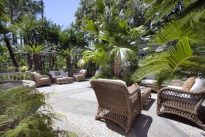 Un espace extérieur aménagé en terrasse, avec des meubles en osier, des palmiers et un sol en pierre.