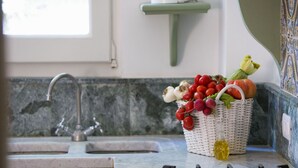 Een keuken met een spoelbak, een mand vol vers fruit en groenten, en een gasfornuis.