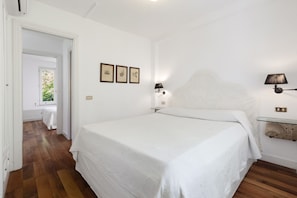Une chambre à coucher avec un grand lit, une table de chevet avec une lampe et une petite étagère ornée d’objets décoratifs.