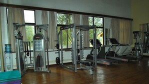Ein Fitnessstudio mit unterschiedlichen Trainingsgeräten, darunter Laufbänder und Kraftgeräte, sowie großen Fenstern mit Vorhängen.