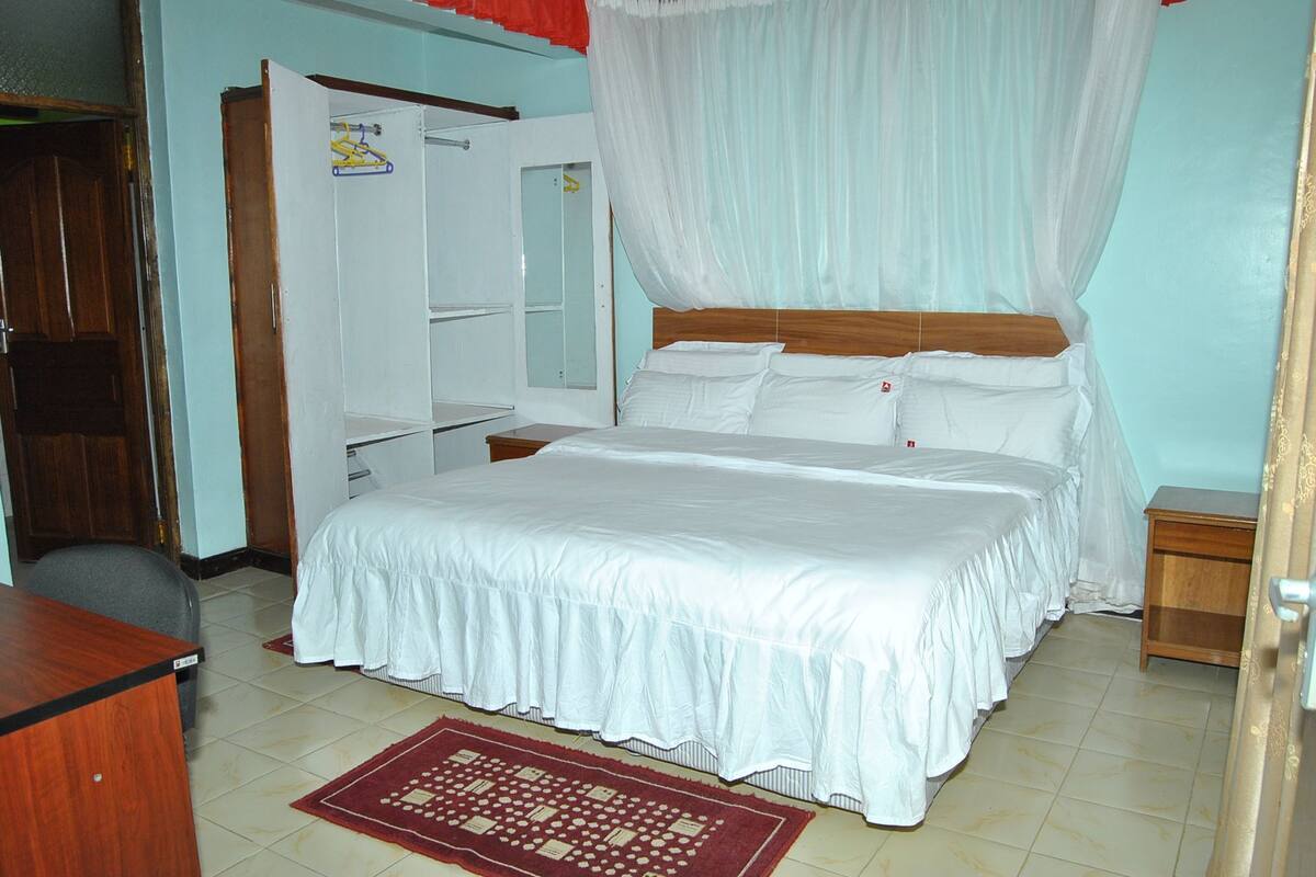 A bedroom with a bed, a wardrobe, a desk, and a mirror.