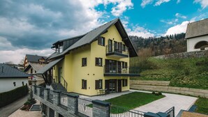 A multi-story yellow building with balconies, a stone retaining wall, and a paved courtyard. - Wellness Paradise Apartment (Bled)