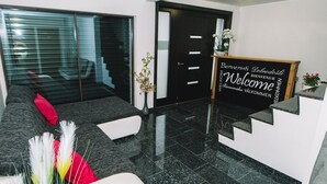 A modern reception area with a black reception desk, a glass door, and a red pillow on a grey sofa. - Wellness Paradise Apartment (Bled)