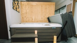 A modern bathroom with a wooden panel wall, a white bathtub, and a black chair. - Wellness Paradise Apartment (Bled)