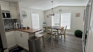 A compact kitchen with white cabinets, a microwave, and a sink. There is a dining area with a table and chairs, and a small trash bin. - Luxury cottage in the heart of paradise (Key Largo)