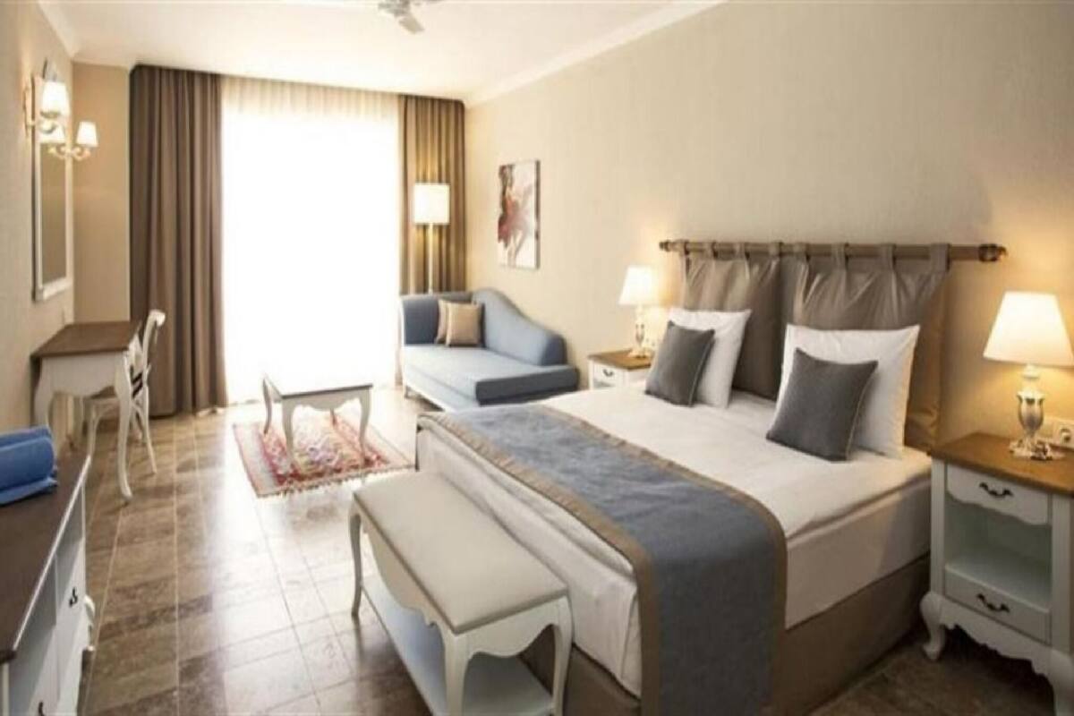 Une chambre d’hôtel équipée d’un lit, d’un bureau, d’une chaise, d’un banc et d’une table de chevet avec des lampes.