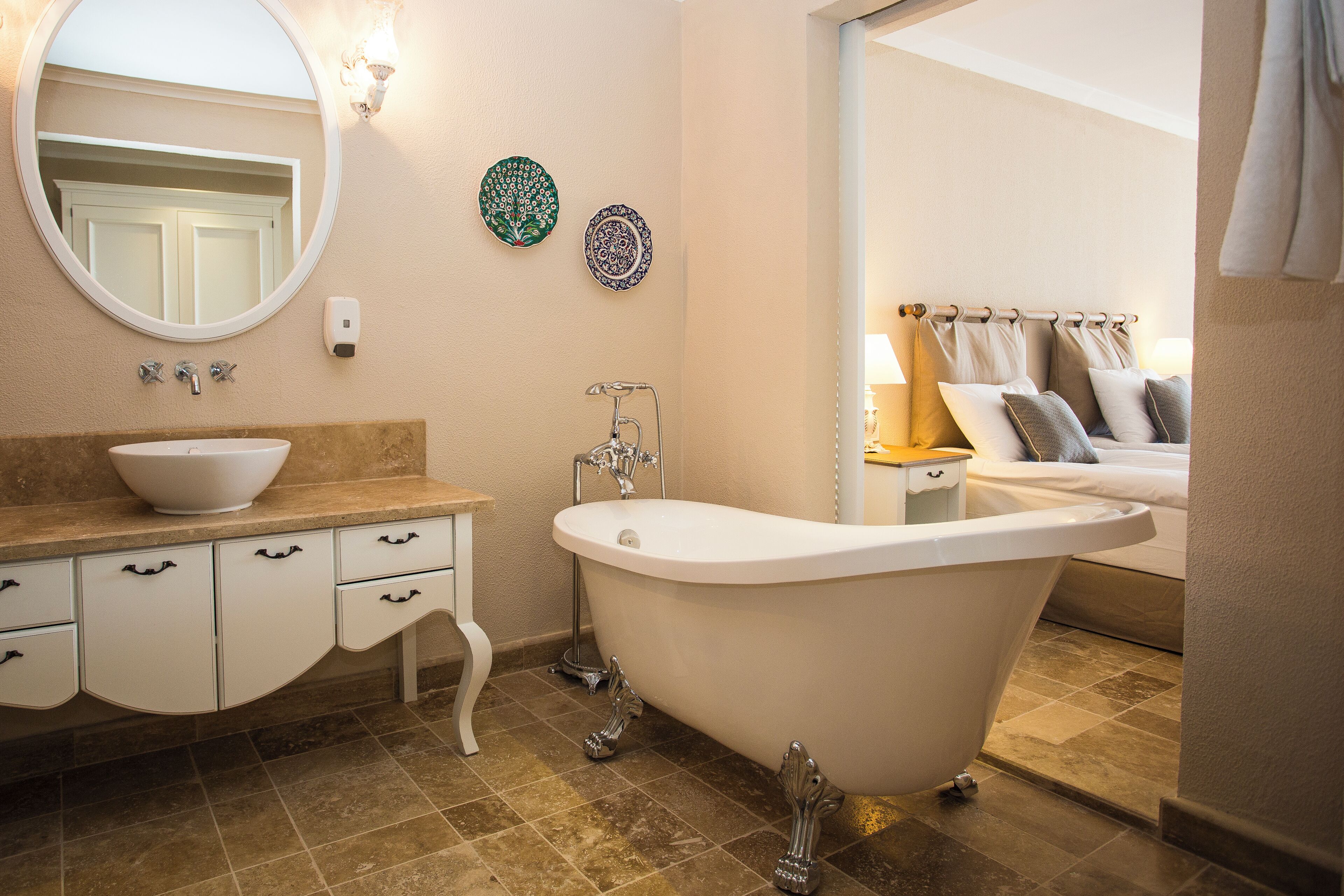 A bathroom with a freestanding bathtub, a sink with a bowl, a mirror, and two decorative plates on the wall.