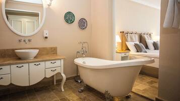 A bathroom with a freestanding bathtub, a sink with a bowl, a mirror, and two decorative plates on the wall.