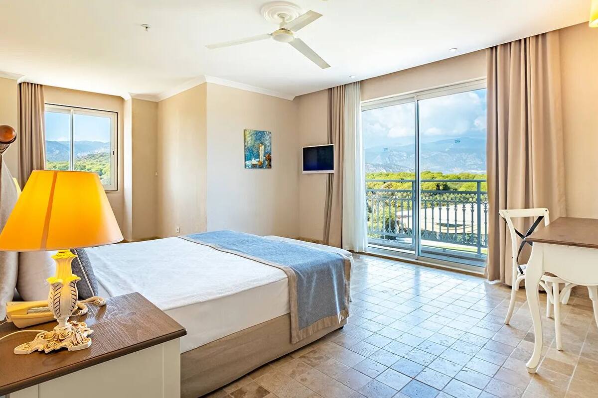 Une chambre d’hôtel avec un lit, un bureau, une chaise, une télévision et un balcon avec vue.
