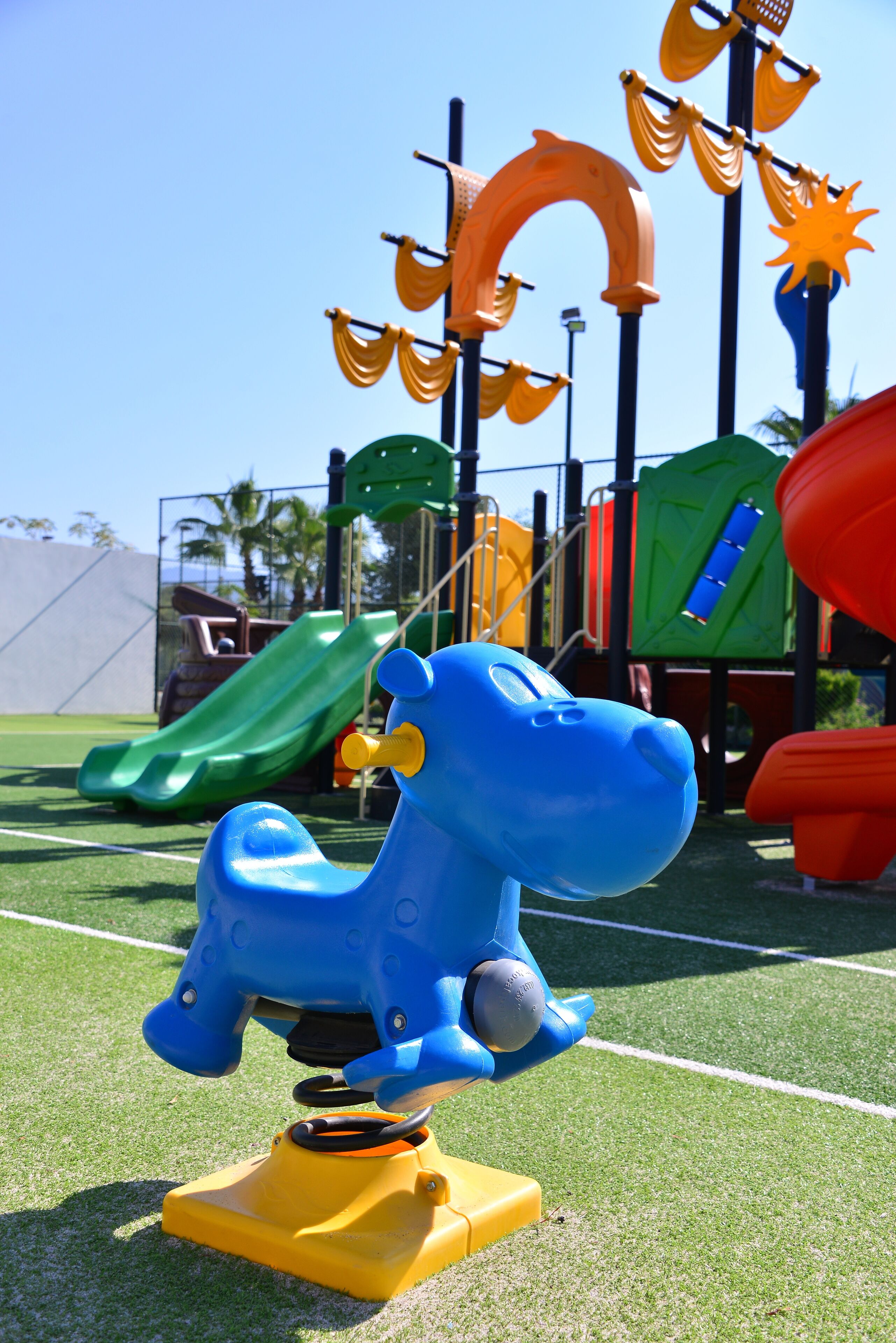 Ein Spielplatz mit einem blauen Pferdeschaukel, einer grünen Rutsche und verschiedenen bunten Spielgeräten.