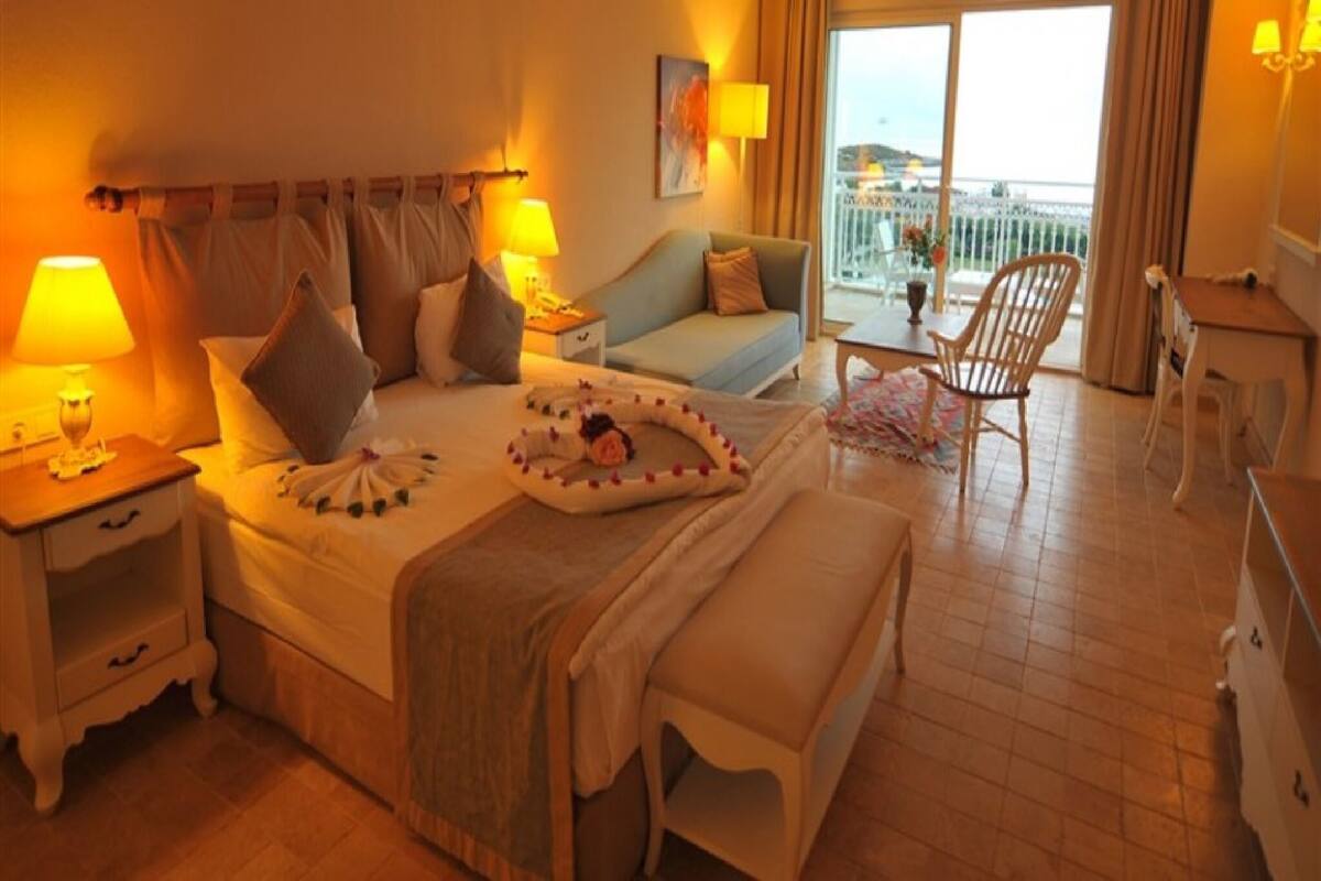 Une chambre d’hôtel comprenant un lit, des tables de chevet, un canapé, un fauteuil et un balcon avec vue.