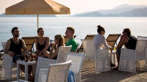 A group of people seated at tables on a deck with a view of the sea and mountains in the background. - Andriake Beach Club Hotel - All Inclusive  (Demre)