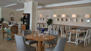 A spacious dining area with round tables and grey upholstered chairs, featuring a central wooden table with a vase and glasses. - Andriake Beach Club Hotel - All Inclusive  (Demre)