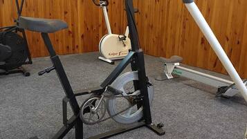 Een sportschool met trainingsapparatuur, waaronder een hometrainer, een loopband en een roeimachine.