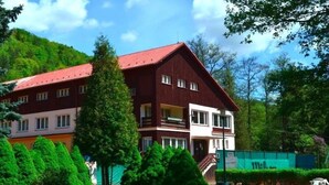 A multi-story building with a red roof and white walls, surrounded by greenery and trees. - Sport Hotel Gejzírpark (Karlovy Vary)