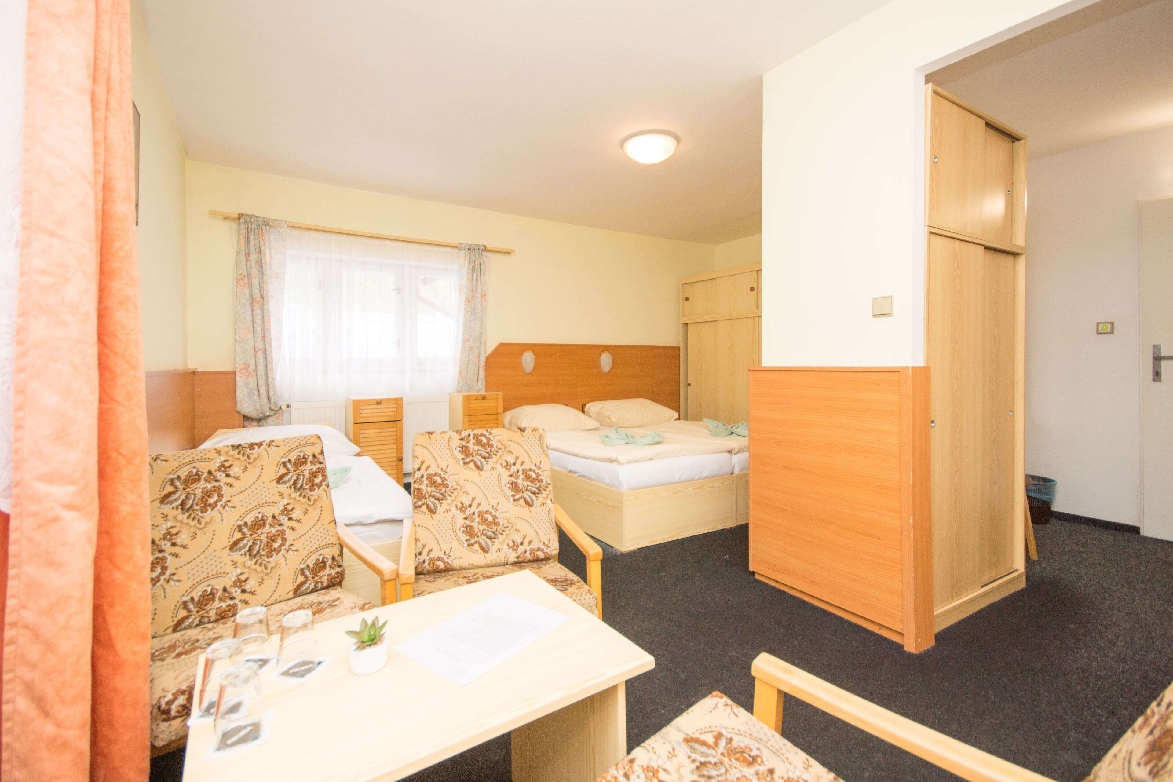 A compact room with a bed, two chairs, a small table, and a wardrobe.