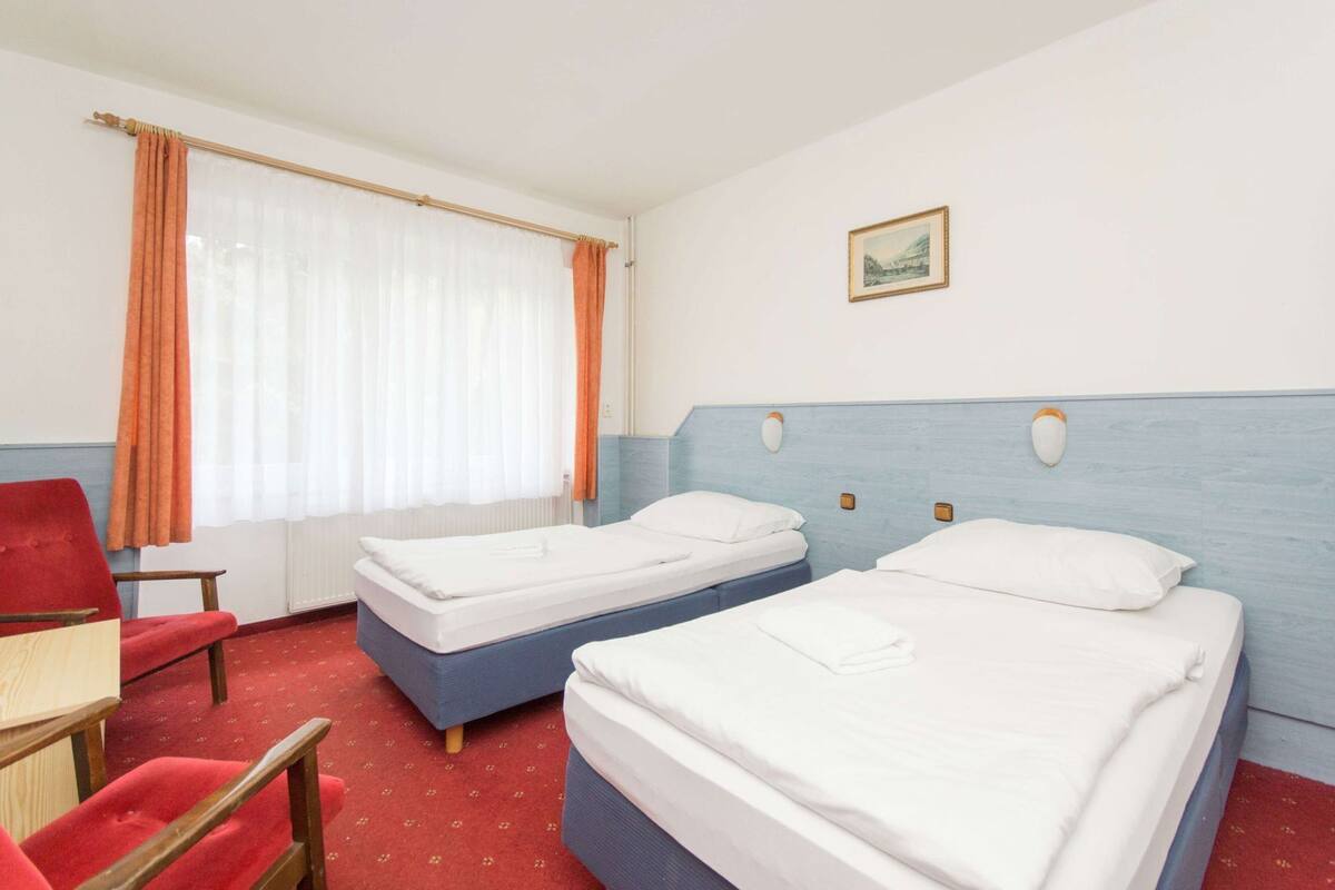 Una habitación de hotel con dos camas, una silla roja, un escritorio de madera y una ventana con cortinas.