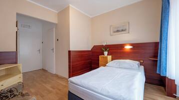 Habitación de hotel con cabecera de madera, cama con ropa de cama blanca, una mesita de noche de madera con una planta y un cuadro en la pared.