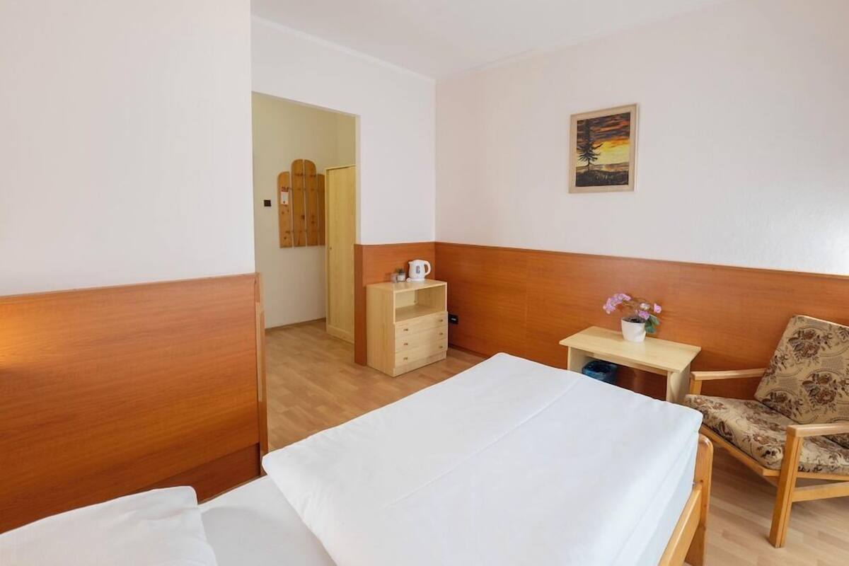 Habitación de hotel con una cama, una silla, una mesita con una taza y flores, y un cuadro en la pared.