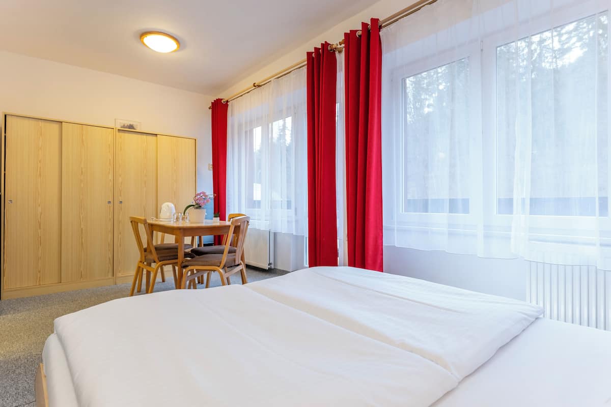 Habitación de hotel con cama, armario de madera, mesa de comedor con sillas y ventana con cortinas rojas.