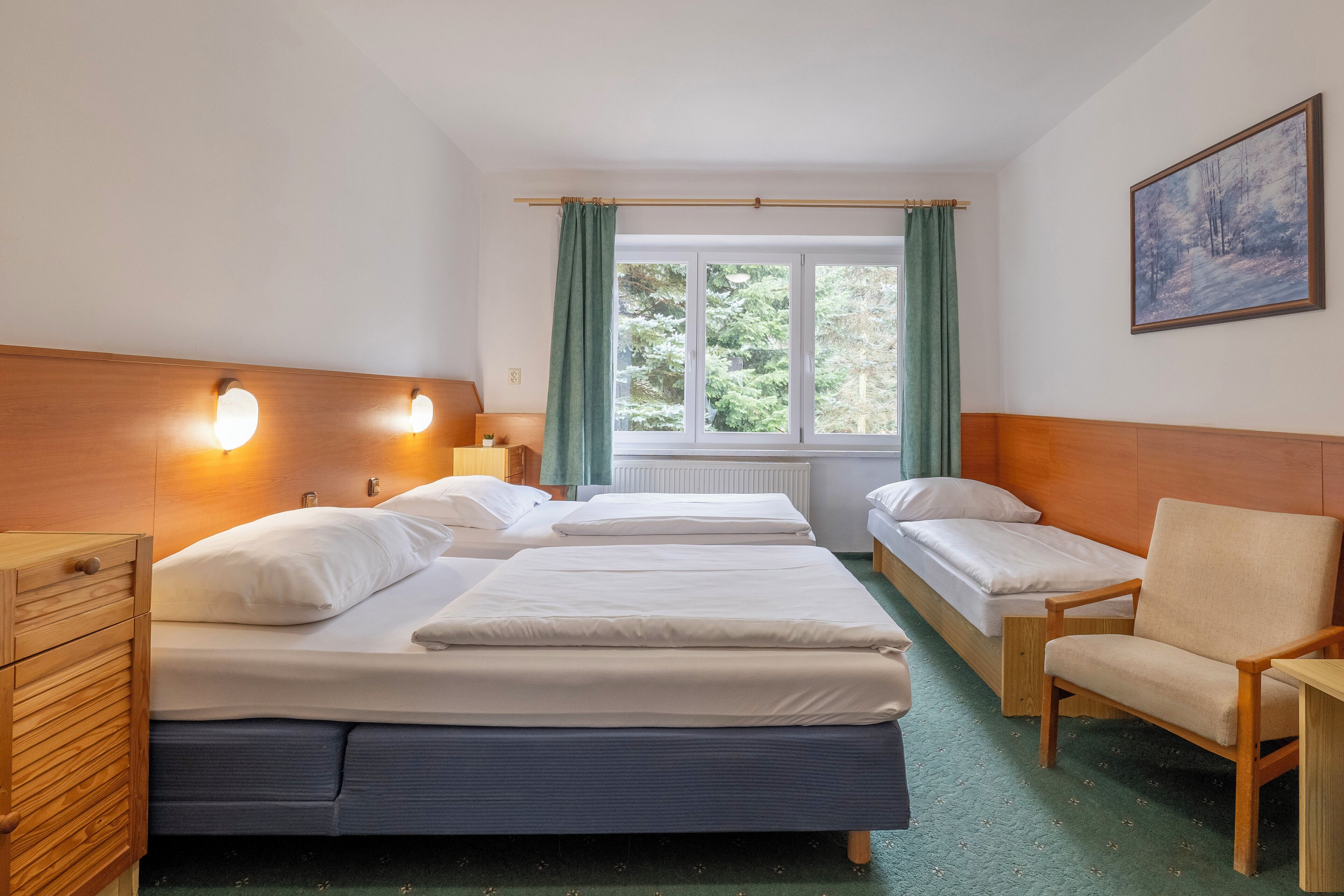Habitación de hotel con dos camas individuales, un aparador de madera, una silla y un ventanal con cortinas.