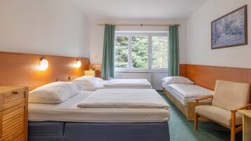 Habitación de hotel con dos camas individuales, un aparador de madera, una silla y un ventanal con cortinas.