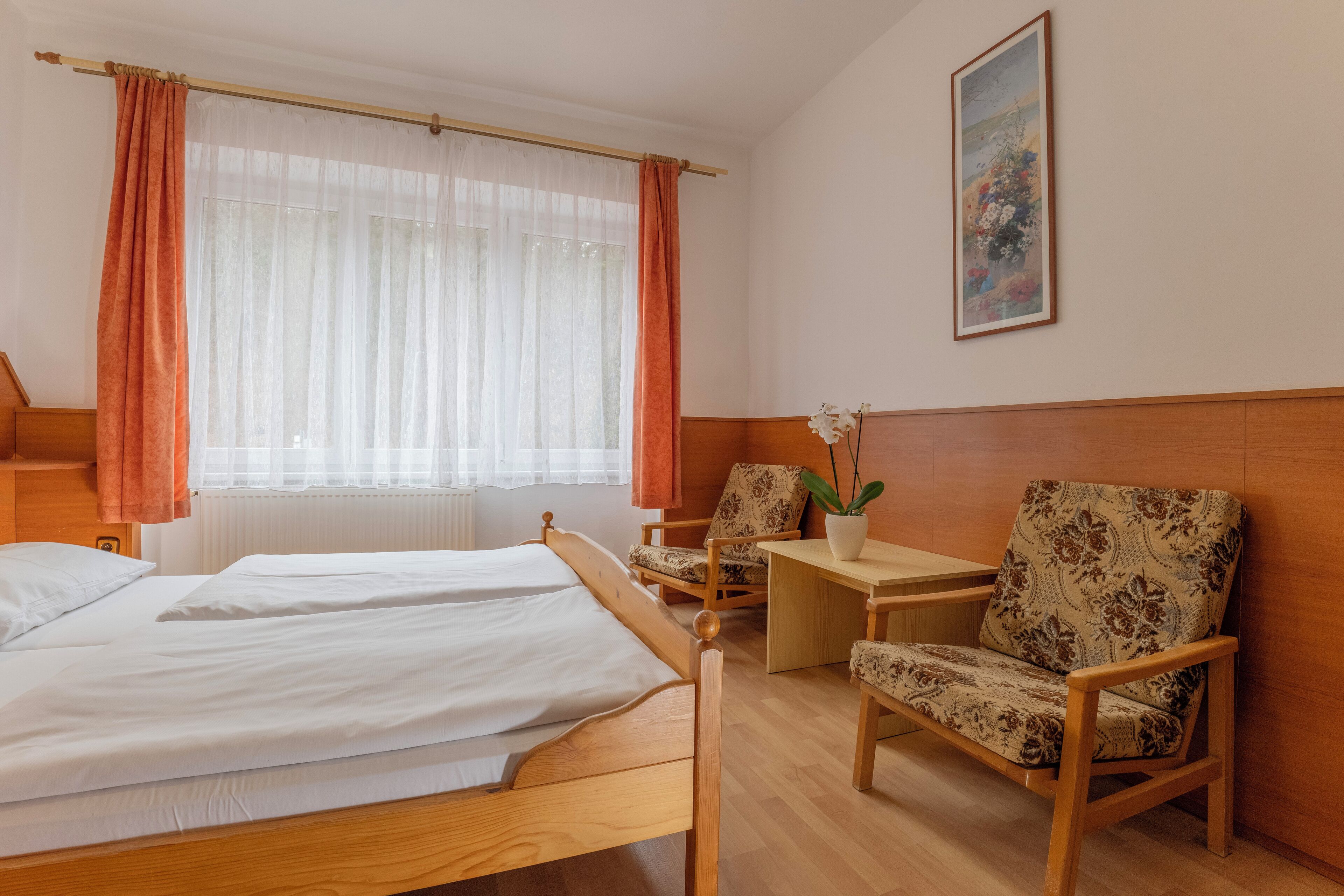 Una habitación de hotel con dos camas de madera, un escritorio de madera, una silla y una planta en maceta.