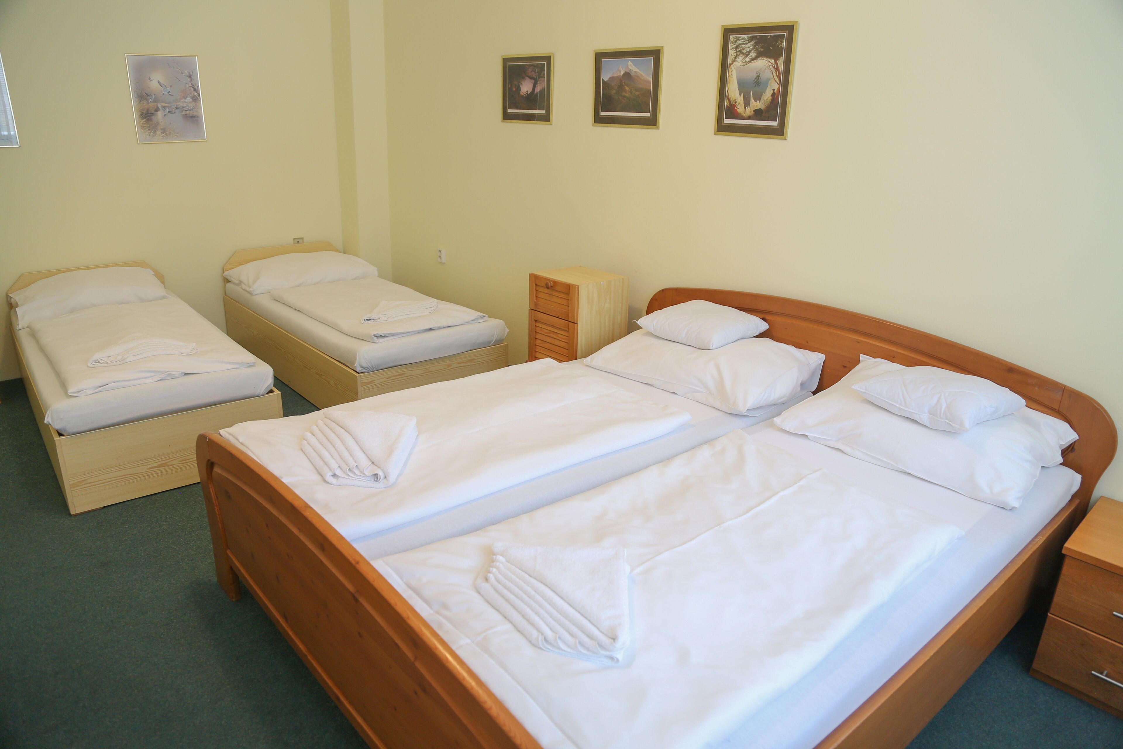 A hotel room with three single beds and one double bed, all neatly made with white linens.