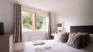 A neatly made bed with folded towels, a bedside table with a lamp, and a window with curtains. - 2 Bedroom Non Sea View Apartment (Scarborough)