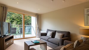 A modern living room with a sofa, a coffee table, a TV on a wooden stand, and a sliding glass door leading to an outdoor area. - 2 Bedroom Non Sea View Apartment (Scarborough)
