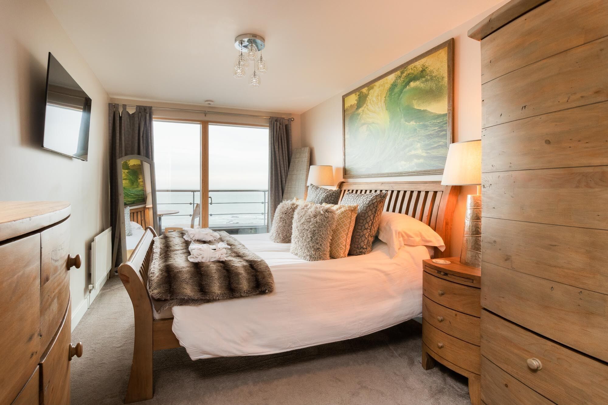 A hotel room with a bed, wooden dresser, and a painting of a landscape.