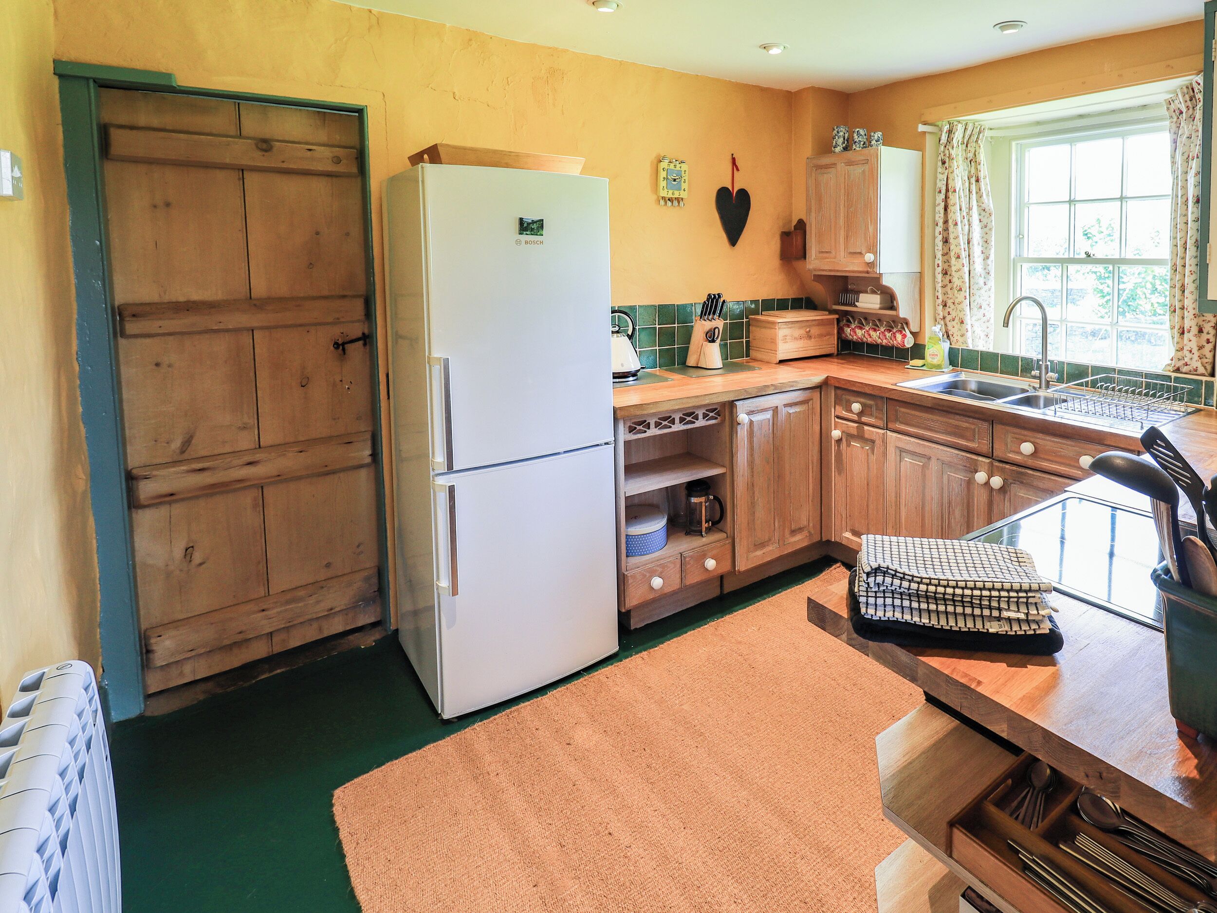 A kitchen with wooden cabinets, a Bosch refrigerator, a window with curtains, and a green floor.