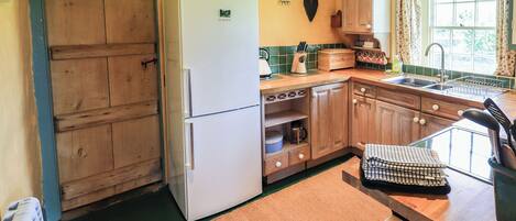 A kitchen with wooden cabinets, a Bosch refrigerator, a window with curtains, and a green floor.